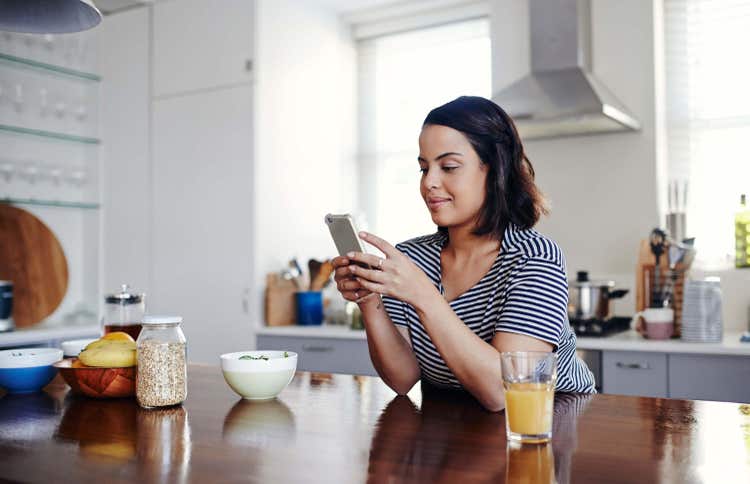 Woman seated in kitchen scrolling her phone